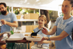 Assistance given by charitable group to less privileged through non-profit initiative, ensures warm meals and essential items for the homeless and needy. Woman at food drive feeding the poor people.